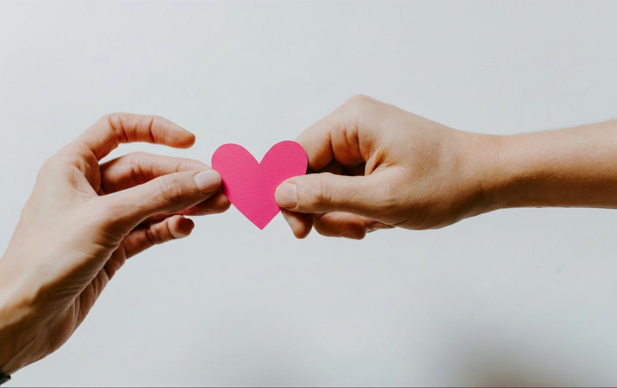 Deux mains se transmettant un cœur rose pour symboliser l’entraide et la coopération