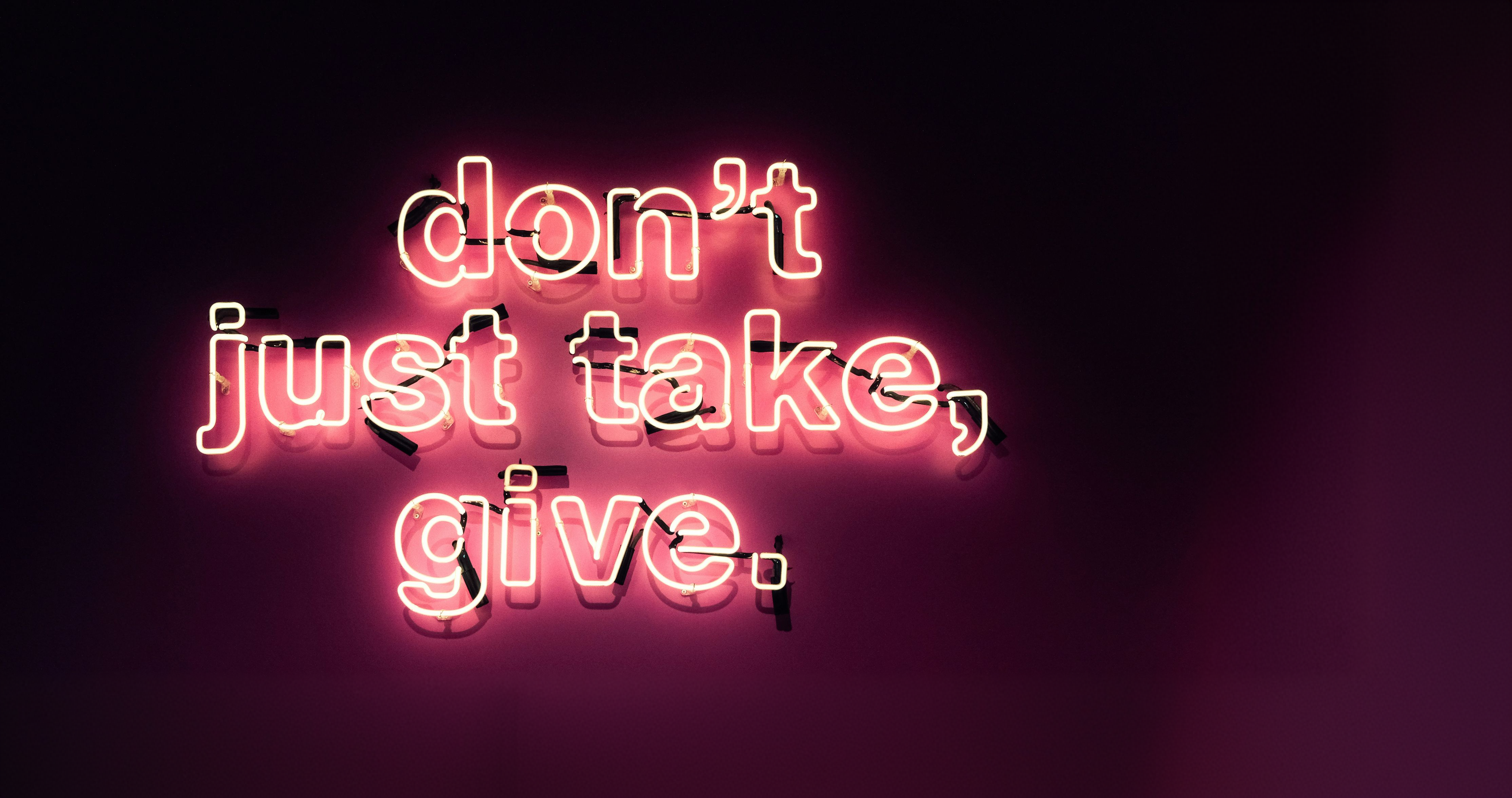 Enseigne lumineuse rose affichant le message don’t just take, give.